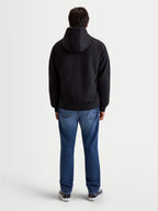 Alpinestars Ageless Hoodie, men's urban motorcycle hoodie in black, rear profile view on a model wearing jeans and casual riding shoes, featuring a fixed hood and protective textile construction.