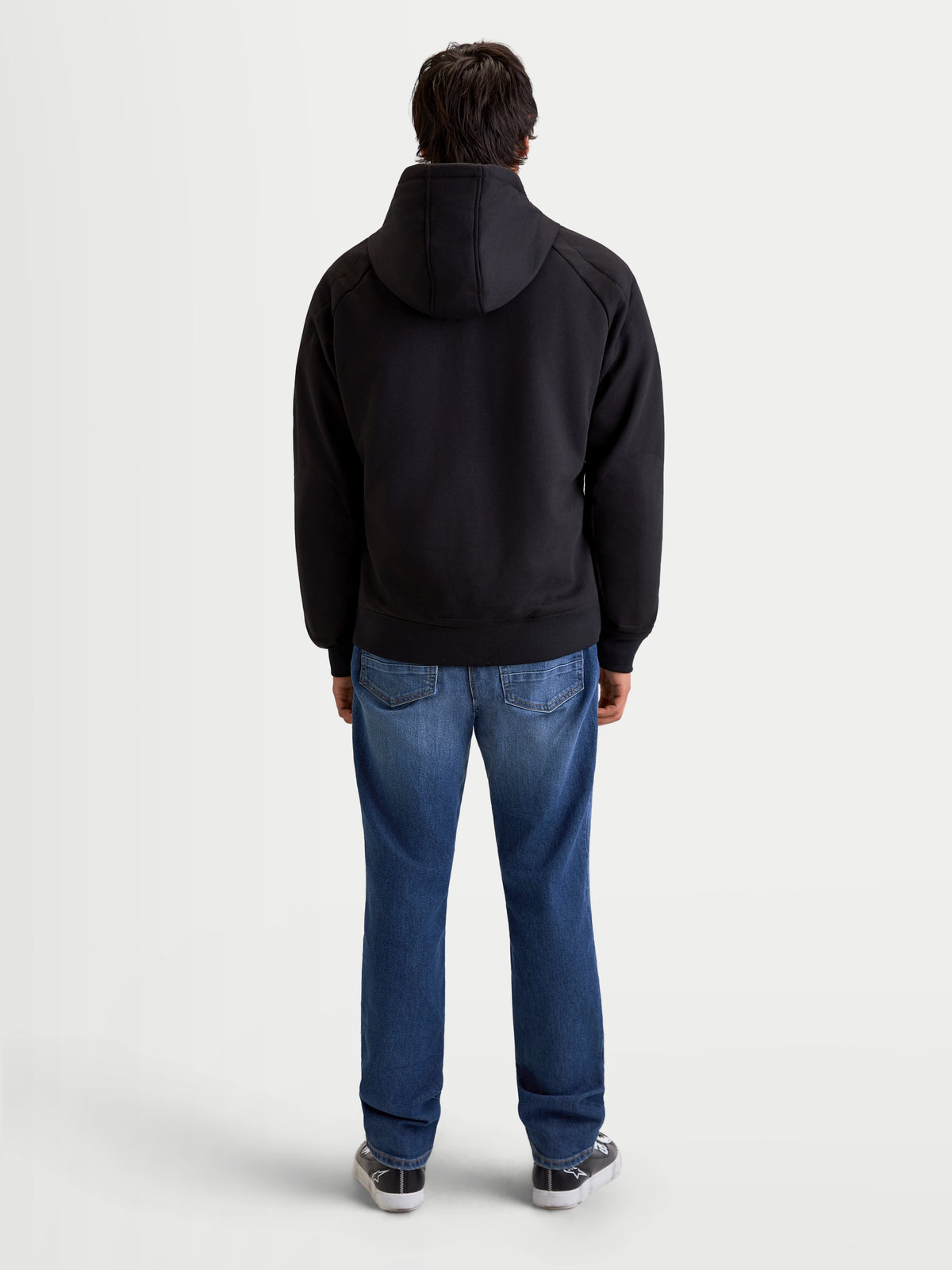 Alpinestars Ageless Hoodie, men's urban motorcycle hoodie in black, rear profile view on a model wearing jeans and casual riding shoes, featuring a fixed hood and protective textile construction.