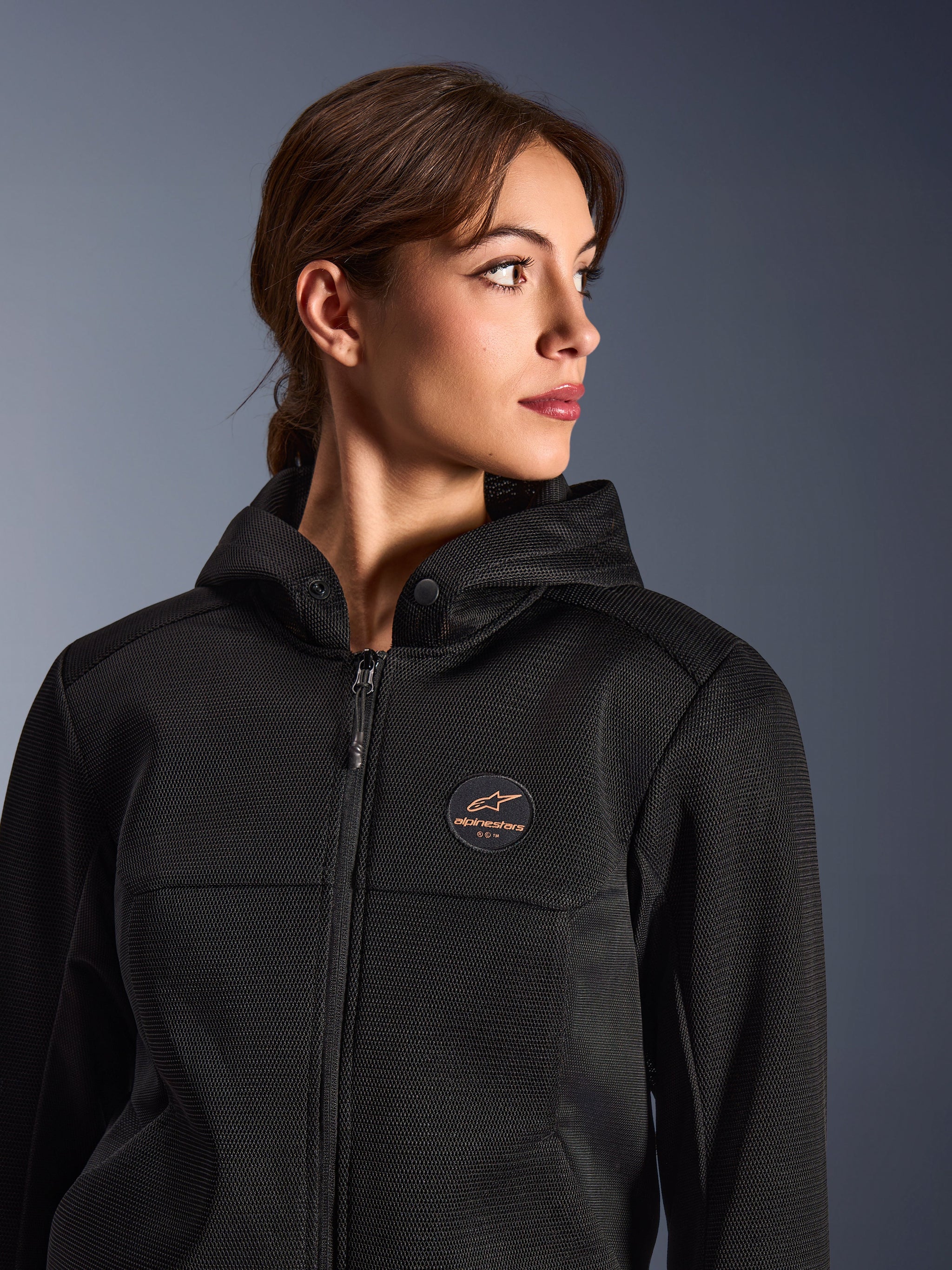Mujer vistiendo la sudadera Alpinestars Stella Chrome Superairflow, negra con logotipo color cobre, construcción en malla 3D para un máximo flujo de aire, equipamiento técnico de moto diseñado para mujer, estilo de conducción deportiva urbana