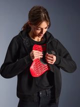 Sudadera Alpinestars Stella Chrome Superairflow, sudadera de moto para mujer, negra, modelo sosteniendo un protector de pecho Nucleon rojo, construcción de malla 3D ligera para conducción urbana y deportiva