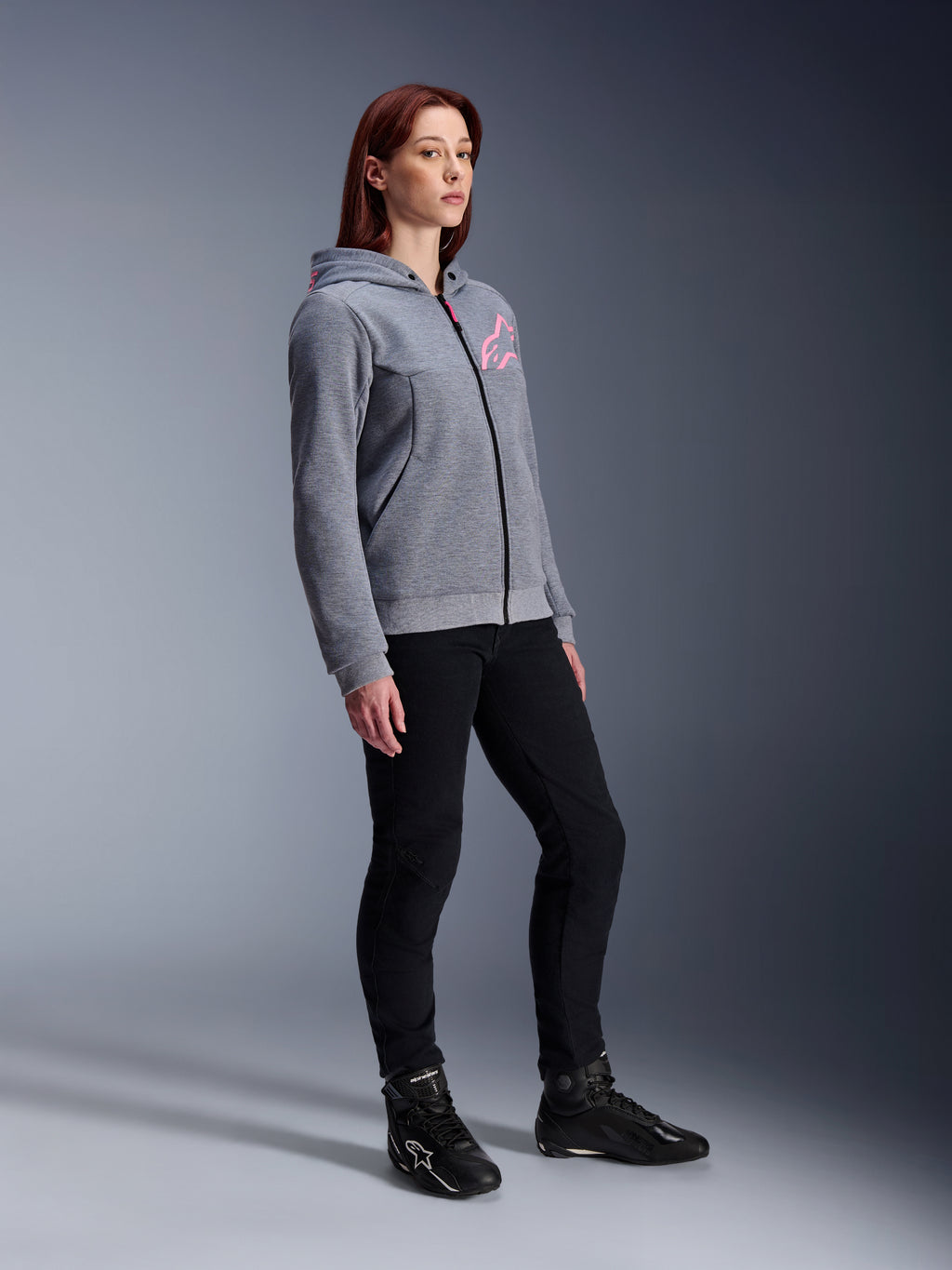 Alpinestars Stella Chrome V2 Sport Hoodie, sudadera de moto para mujer, gris jaspeado y rosa flúor, combinada con pantalones de conducción negros y botas negras, equipamiento de conducción urbana casual