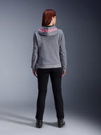Alpinestars Stella Chrome V2 Sport Hoodie, sudadera de moto para mujer, gris jaspeado y rosa flúor, vista posterior que muestra el logotipo rosa de Alpinestars en la capucha, combinada con pantalones de conducción negros y botas, ropa de moto casual para mujer