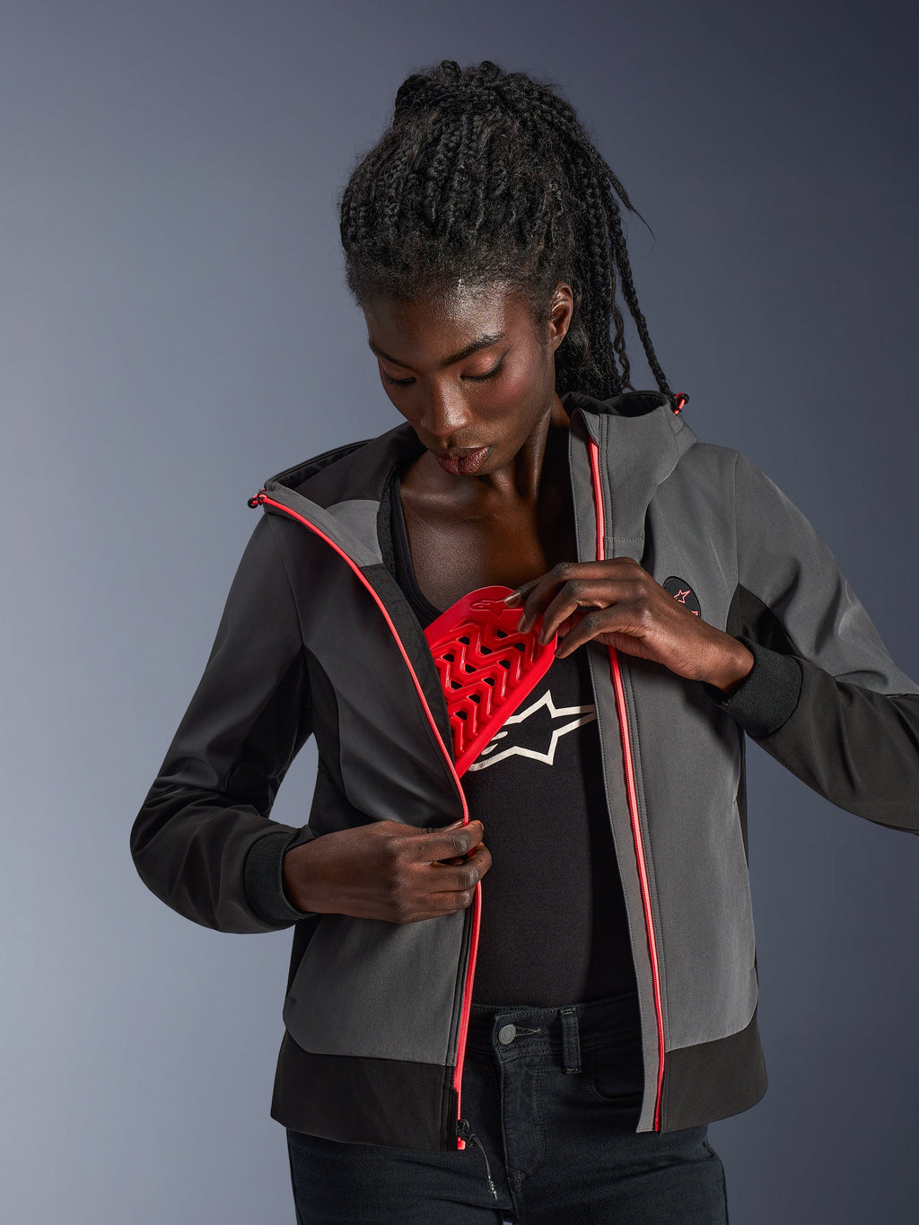 Sudadera Alpinestars Stella Radium Tech para mujer en gris oscuro y negro, modelo demostrando la protección roja Nucleon Flex Plus desmontable, sudadera urbana para motociclismo con detalles de cremallera en rosa.