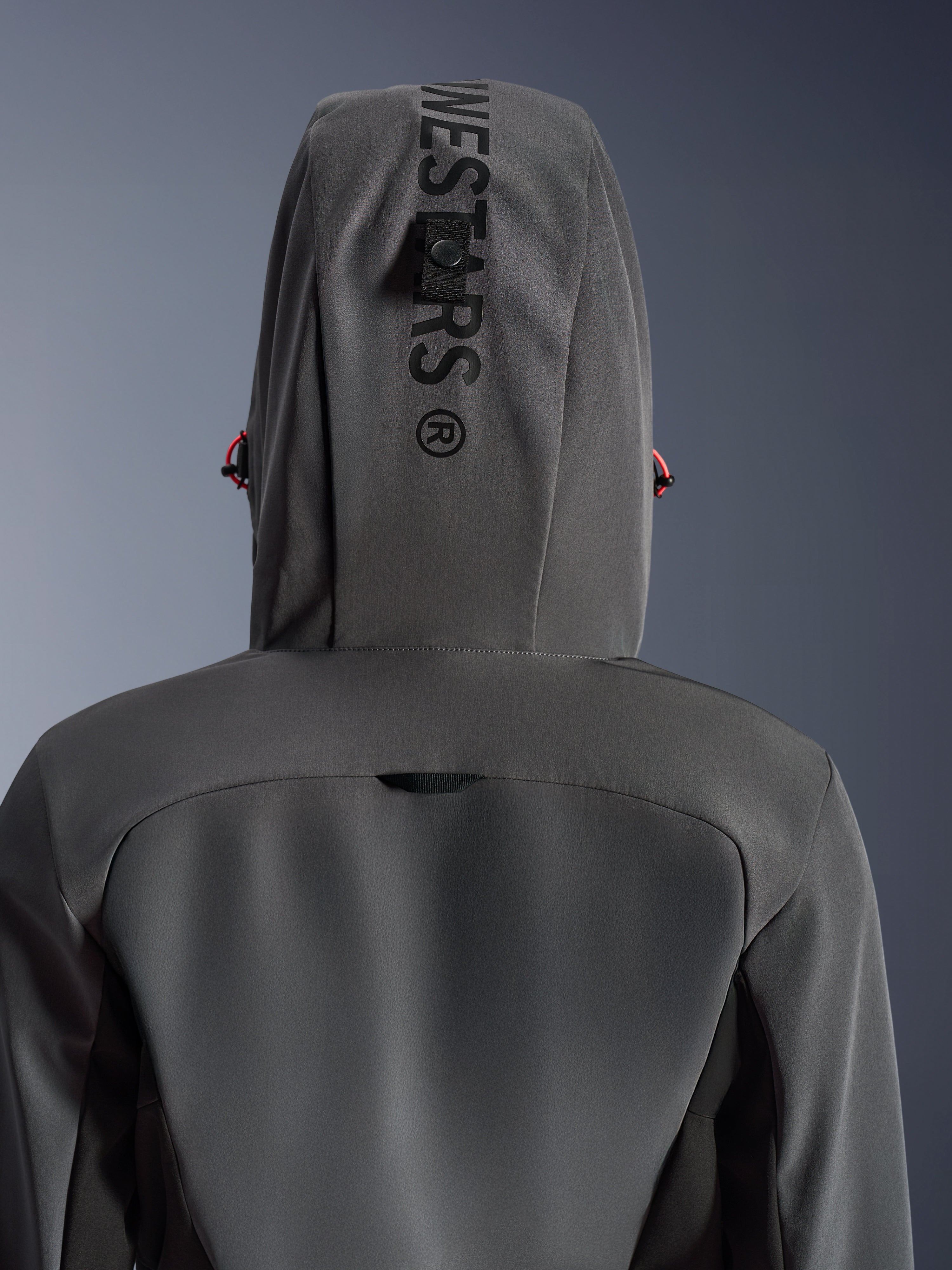 Alpinestars Woman Stella Radium Tech Hoodie, Gris Oscuro Negro, vista posterior de cerca que muestra la capucha con marca vertical y bucle de sujeción, detalles de cordones rojos, construcción textil duradera de 3 capas cortavientos para conducción urbana en moto.