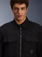 Alpinestars Bryon Water Resistant Overshirt, negra, vista de primer plano de la cremallera frontal y los bolsillos del pecho, textura de lona encerada duradera, diseño urbano minimalista con detalles de la marca y etiqueta de logotipo tejida