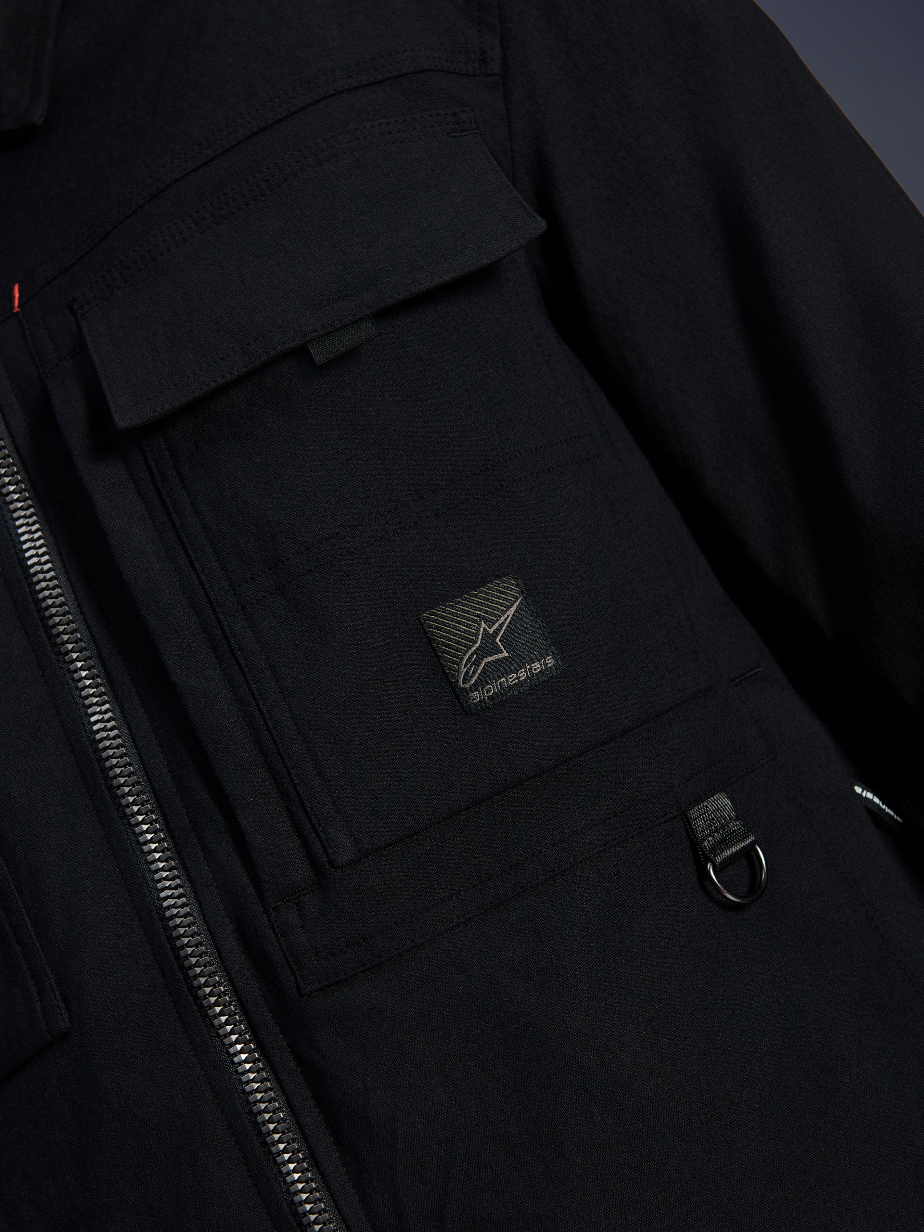 Alpinestars Bryon Water Resistant Overshirt, negro, primer plano del tejido de lona encerada, cremallera frontal, bolsillo tipo cargo en el pecho con parche del logotipo de Alpinestars y detalle de anilla metálica en D