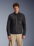 Sobrecamisa Alpinestars Bryon Water Resistant, negra, chaqueta de moto urbana con diseño inspirado en la ropa de trabajo, cuenta con dos grandes bolsillos cargo en el pecho y cremallera completa, confeccionada en lona encerada, vestida por un modelo con pantalones cargo beige para un look utilitario contemporáneo.