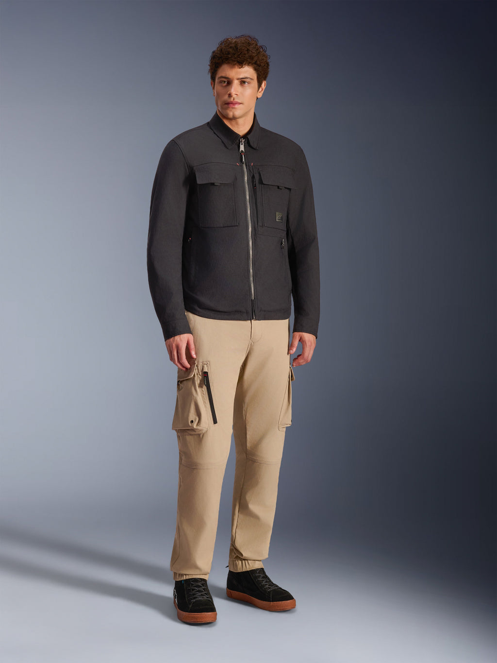 Alpinestars Bryon Water Resistant Overshirt, negra, modelo masculino con pantalones cargo caqui y calzado negro, chaqueta de moto urbana con diseño inspirado en la ropa de trabajo, toma de estudio de cuerpo completo