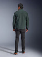 Sobrecamisa Alpinestars Bryon resistente al agua en color Dark Emerald, vista trasera en modelo, combinada con pantalones de moto gris oscuro y calzado de conducción negro, mostrando un diseño clásico inspirado en la ropa de trabajo con una parte trasera ligeramente más larga para mayor cobertura al conducir.