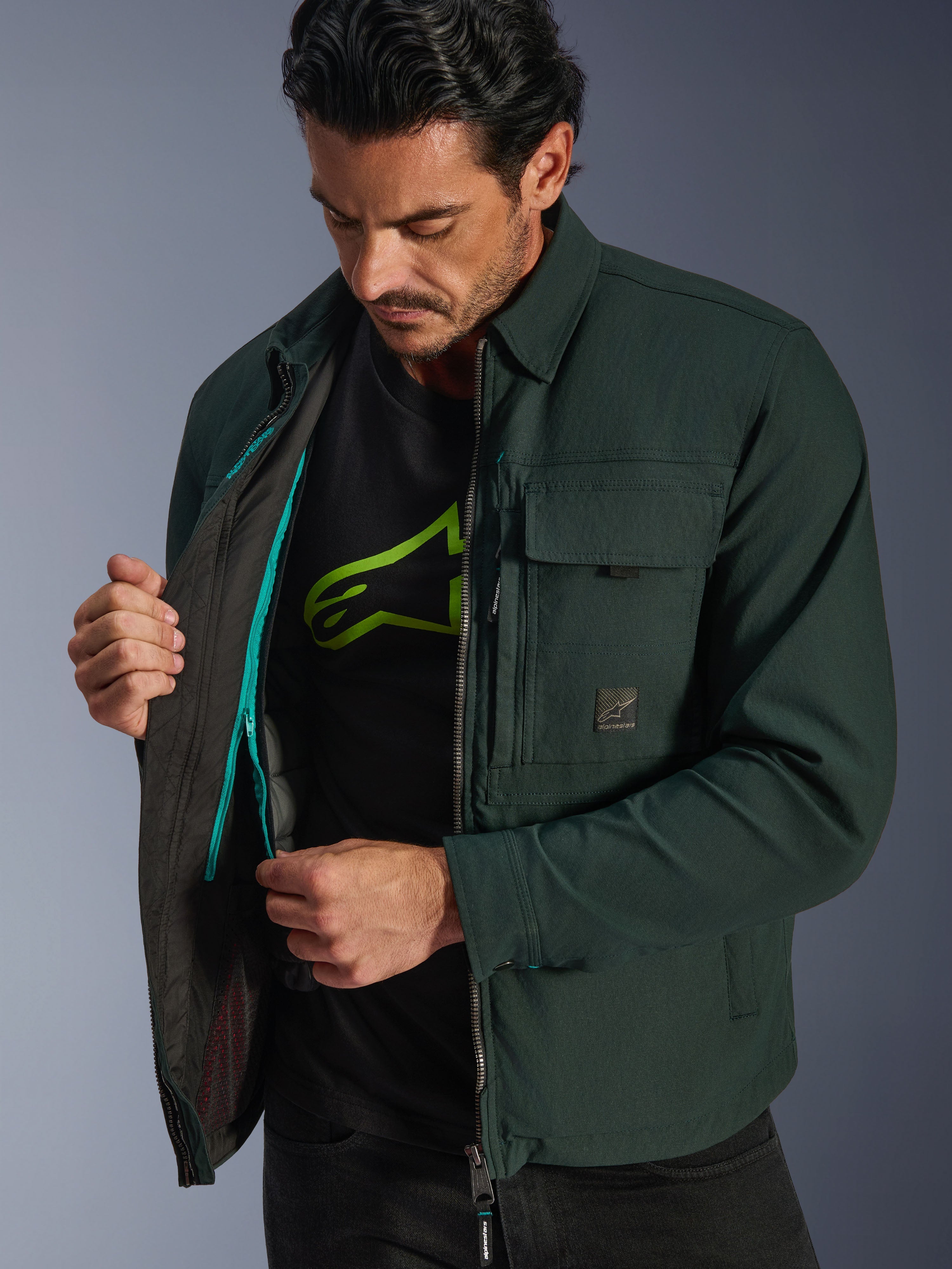 Alpinestars Bryon Water Resistant Overshirt, Dark Emerald, vista lifestyle del modelo revelando el chaleco térmico interior y el detalle de la cremallera verde azulado, chaqueta de moto urbana de lona encerada con bolsillos cargo