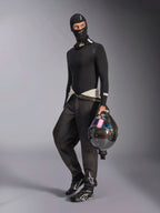 Pasamontañas Alpinestars ZX Evo V3, negro, usado por un piloto con equipo completo de capas base para automovilismo, con el logo blanco en la frente, sosteniendo un casco de fibra de carbono con visera iridiscente, ropa profesional de automovilismo resistente al fuego.