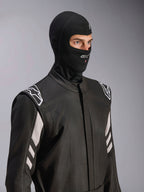Pasamontañas Alpinestars ZX Evo V3, negro, sotocasco ignífugo para automovilismo, usado por un modelo con un traje de carreras negro con detalles blancos, incluye el logotipo de Alpinestars en la barbilla, puerto para tubo de hidratación y equipo de protección profesional para deportes de motor