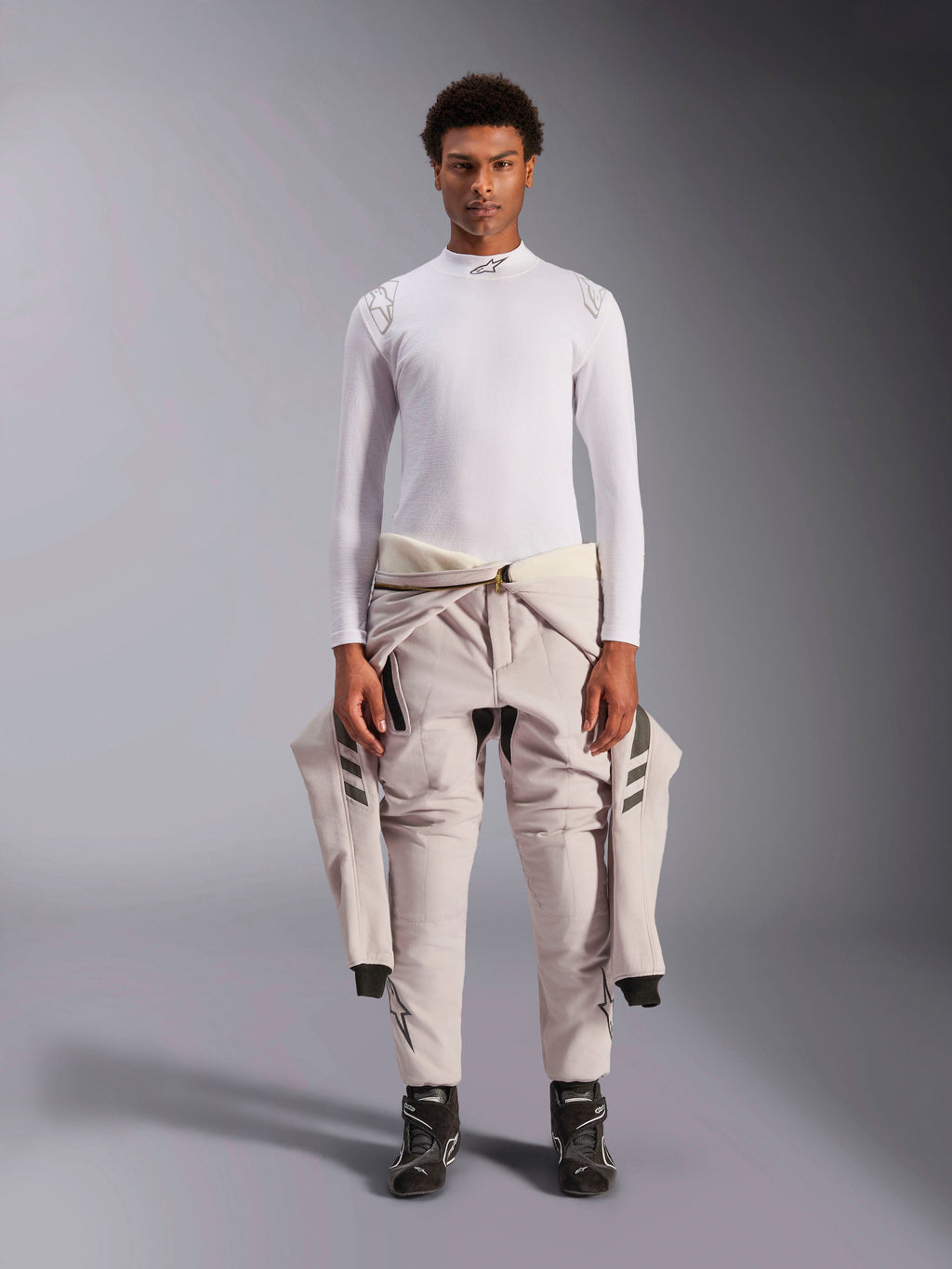 Alpinestars ZX Evo V3 Top, manga larga, blanco, capa base de automovilismo usada con un traje de carreras de color claro atado a la cintura y botas de carreras negras, con cuello alto con logo y marca en los hombros, ropa interior técnica profesional resistente a las llamas