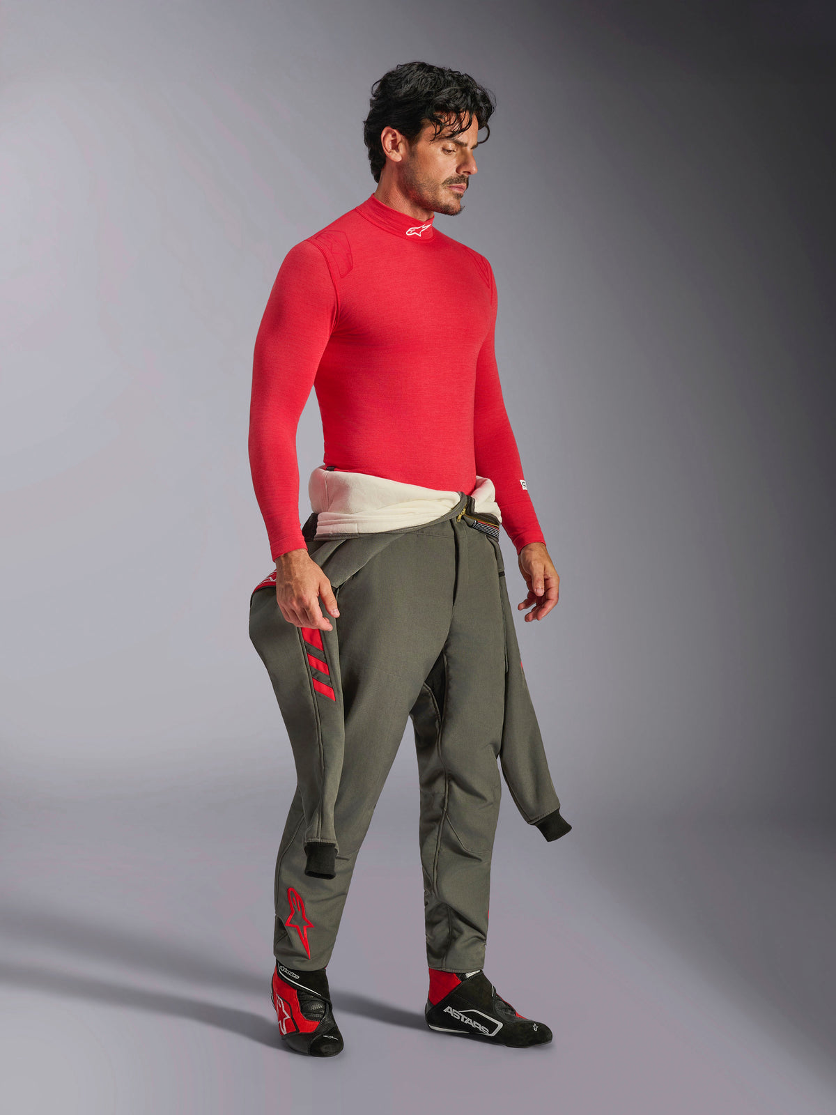 Alpinestars ZX Evo V3 Long Sleeve Top en rojo, capa base de automovilismo resistente al fuego, usada con pantalones de carreras verde oliva y calzado de carreras negro y rojo, equipamiento profesional de automovilismo, retrato de estudio