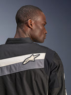 Chaqueta Alpinestars T-Dyno WR, chaqueta textil para moto, negro, gris oscuro y crudo, primer plano de la parte superior de la espalda y el hombro con franjas horizontales y logotipo de la estrella de Alpinestars, usada por un modelo, diseño de inspiración heritage para conducción en carretera