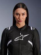 Modelo femenina vistiendo la chaqueta Alpinestars Stella T-SPS Air V2, chaqueta de moto para mujer, negra y blanca, con paneles de malla transpirable y logo de Alpinestars blanco en el pecho, diseño deportivo para conducción en carretera