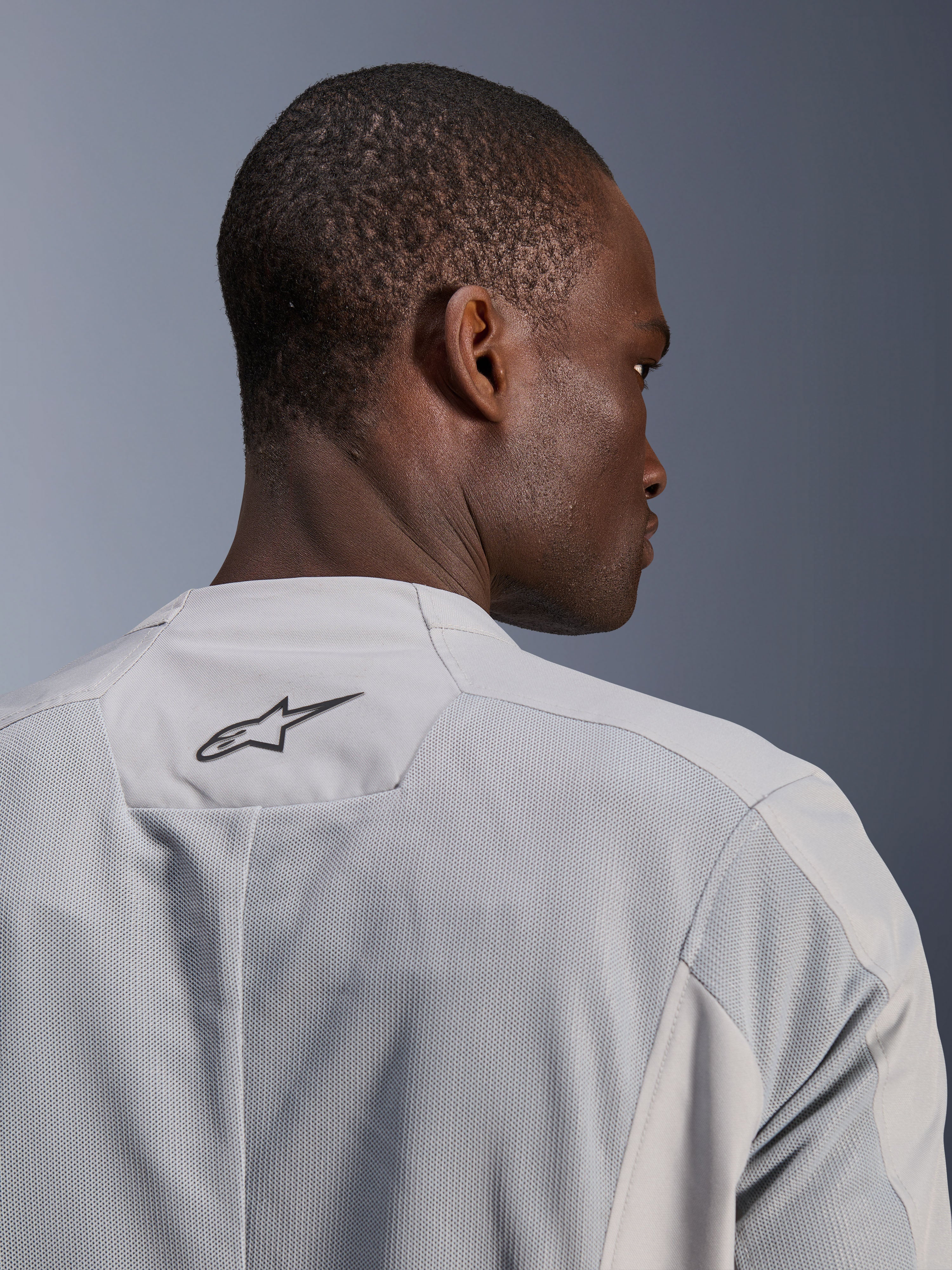 Chaqueta Alpinestars C-1 Air, chaqueta de moto textil gris plateado, vista de primer plano desde la espalda con paneles de malla técnica para flujo de aire y un logotipo negro de Alpinestars en la parte superior, estética de motociclista urbano