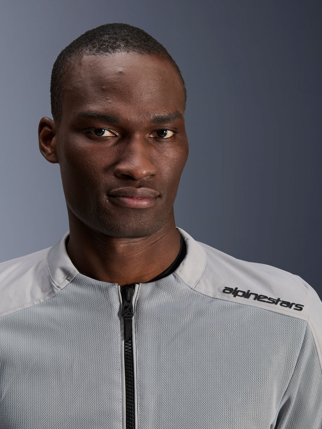 Alpinestars C-1 Air Jacket en plata y gris, retrato en primer plano de un motociclista, con paneles de malla técnica y logotipo negro en el hombro, equipamiento de moto urbano contemporáneo