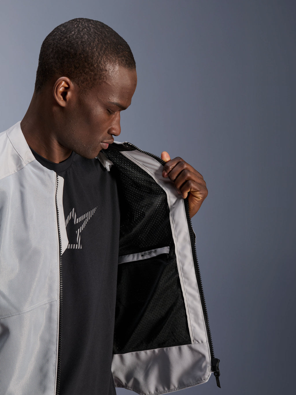 Modelo masculino vistiendo la chaqueta Alpinestars C-1 Air en color plateado, abriendo la parte delantera para mostrar el forro interior de malla técnica negra y el bolsillo interior impermeable con cremallera.