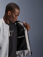 Modelo masculino vistiendo la chaqueta Alpinestars C-1 Air en color plateado, abriendo la parte delantera para mostrar el forro interior de malla técnica negra y el bolsillo interior impermeable con cremallera.