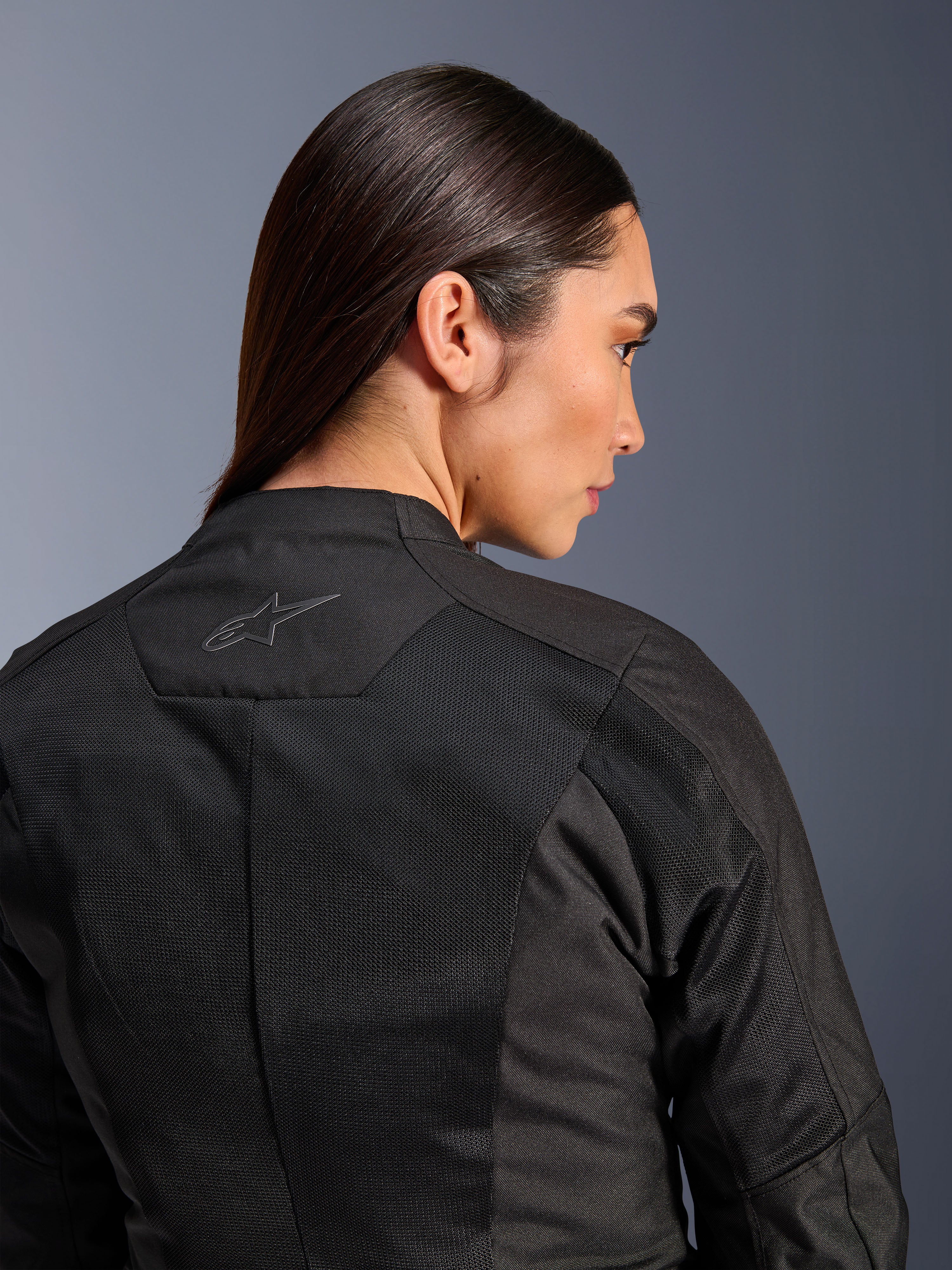 Chaqueta Alpinestars Stella C-1 Air para mujer, chaqueta de moto textil, negra, vista trasera en primer plano que muestra paneles de ventilación de malla técnica y un logotipo de estrella reflectante en la parte superior de la espalda, equipamiento moderno para conducción urbana