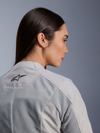 Mujer vistiendo la chaqueta Stella C-1 Air de Alpinestars en color plateado, vista lateral-posterior de primer plano que muestra el logotipo negro de Alpinestars, paneles de ventilación de malla técnica y un diseño de moto urbano, limpio y contemporáneo.