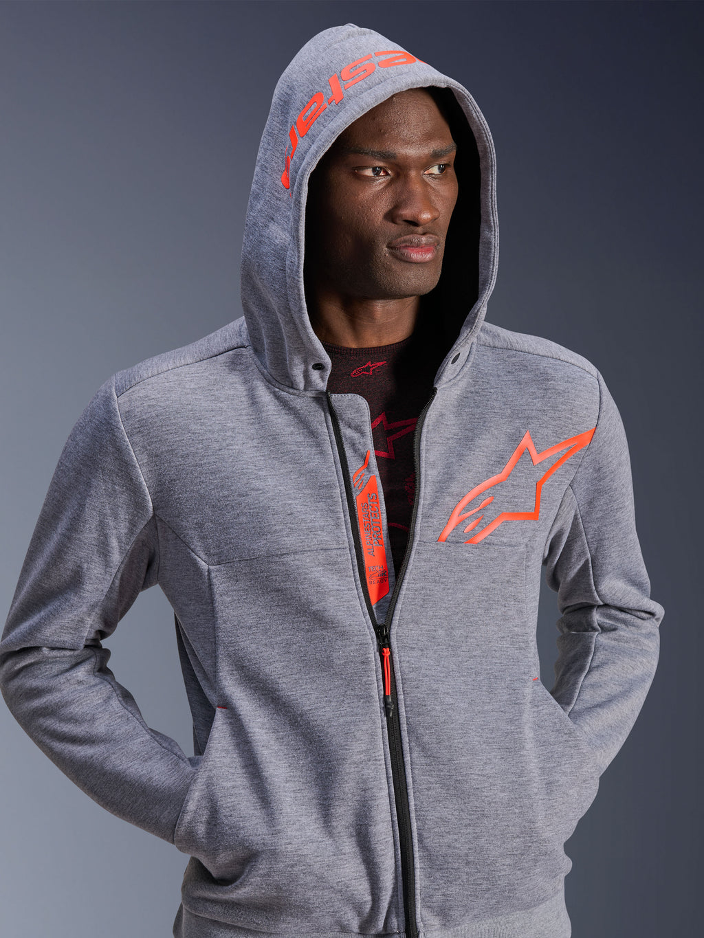 Alpinestars Chrome V2 Sport Hoodie, motorcycle riding gear, Gray Heather and Red Fluo, man wearing hood up, featuring large orange star logo on chest and Alpinestars text on hood, casual urban design