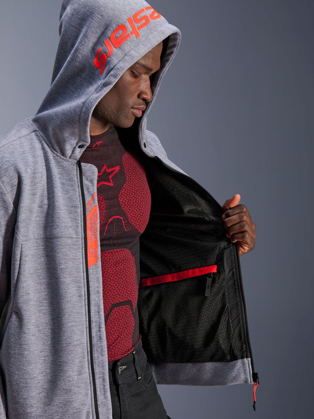 Alpinestars Chrome V2 Sport Hoodie, Motorcycle Hoodie, Gray Heather and Red Fluo, male model showing internal black mesh lining and red waterproof pocket, featuring red branding on the hood and Tech-Air Ready label, casual athletic silhouette for urban riding