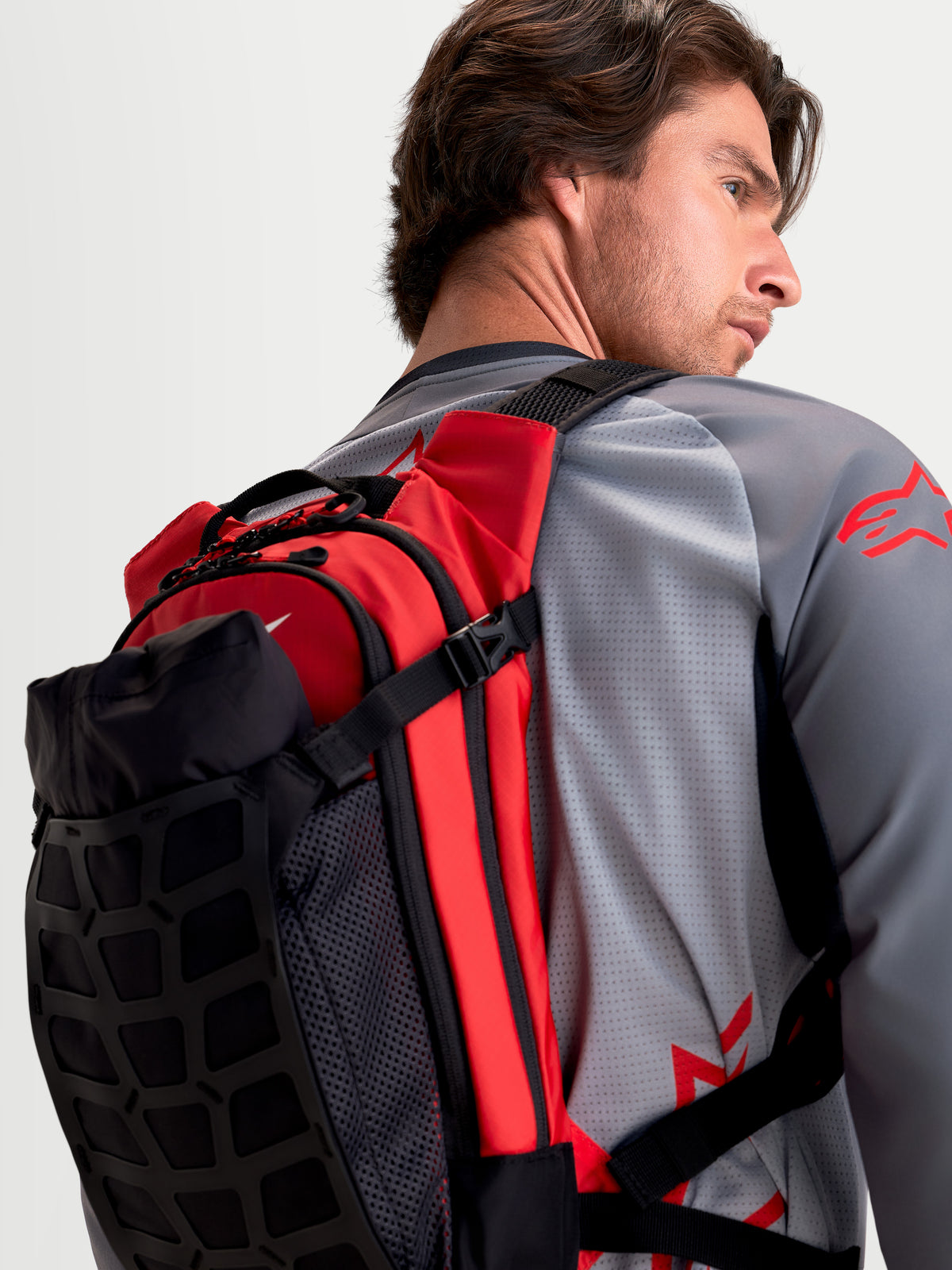 Alpinestars AT-9 Backpack, motocross backpack in black and bright red, rear profile view worn by a model showcasing lightweight textile construction and padded shoulder straps.