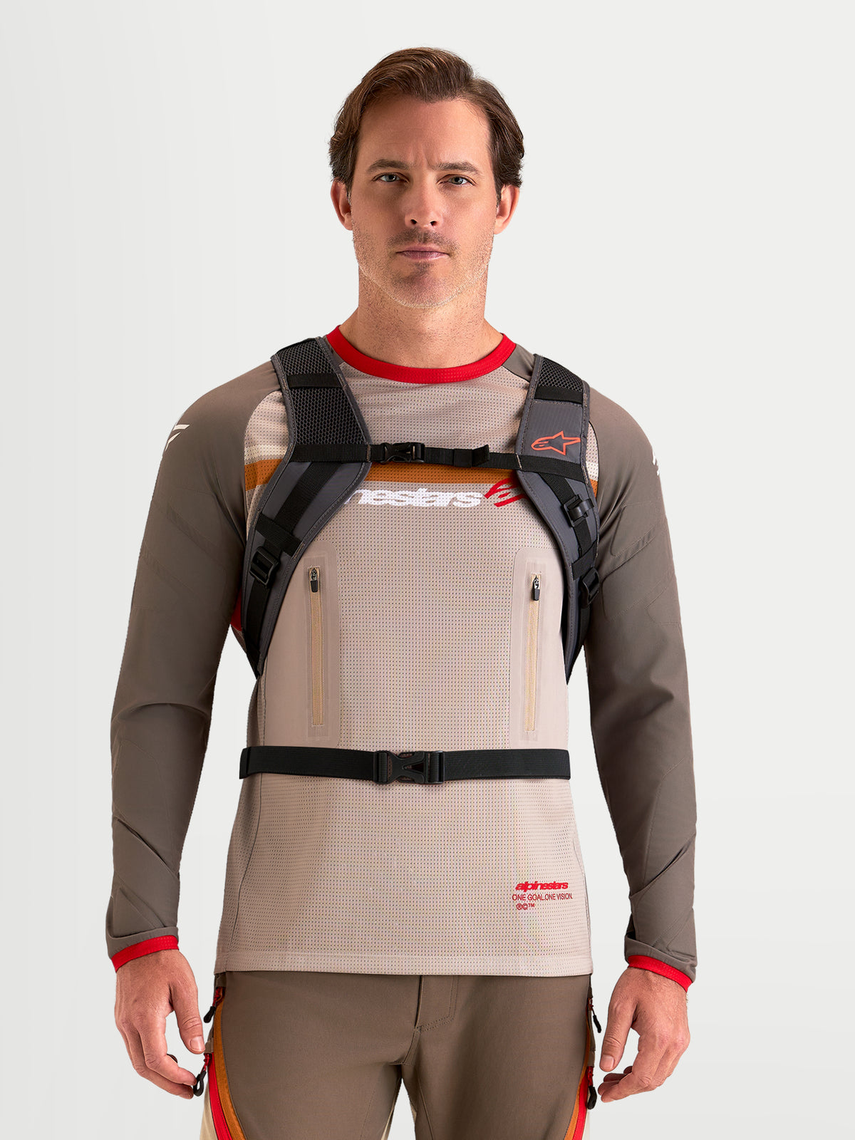 Alpinestars Mochila AT-9, mochila de motocross en color marrón y gris oscuro, vista frontal en un modelo que lleva un arnés de hombros acolchado y un sistema de correas con hebilla
