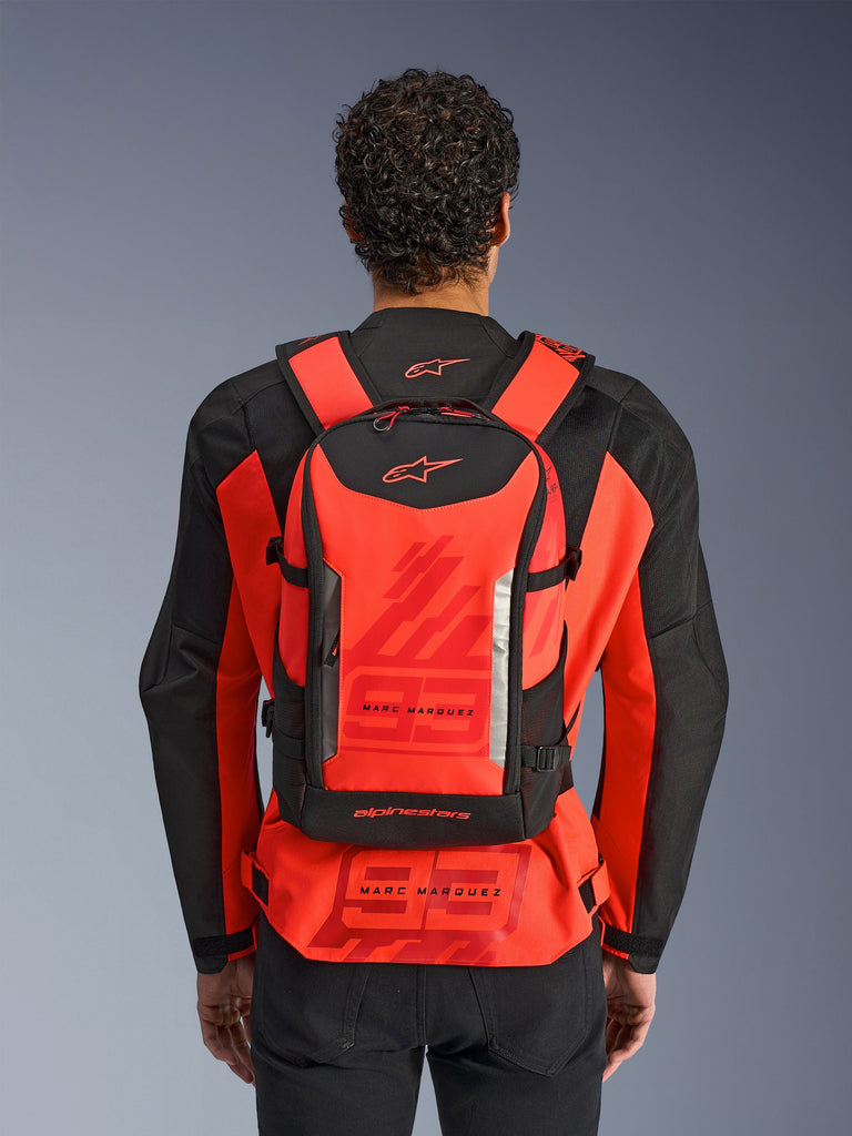 Mochila Alpinestars MM93 AMP3, mochila técnica para moto, rojo flúor y negro, llevada por un piloto desde atrás sobre una chaqueta de carreras MM93 roja y negra a juego, con logotipos de Marc Márquez y Alpinestars.
