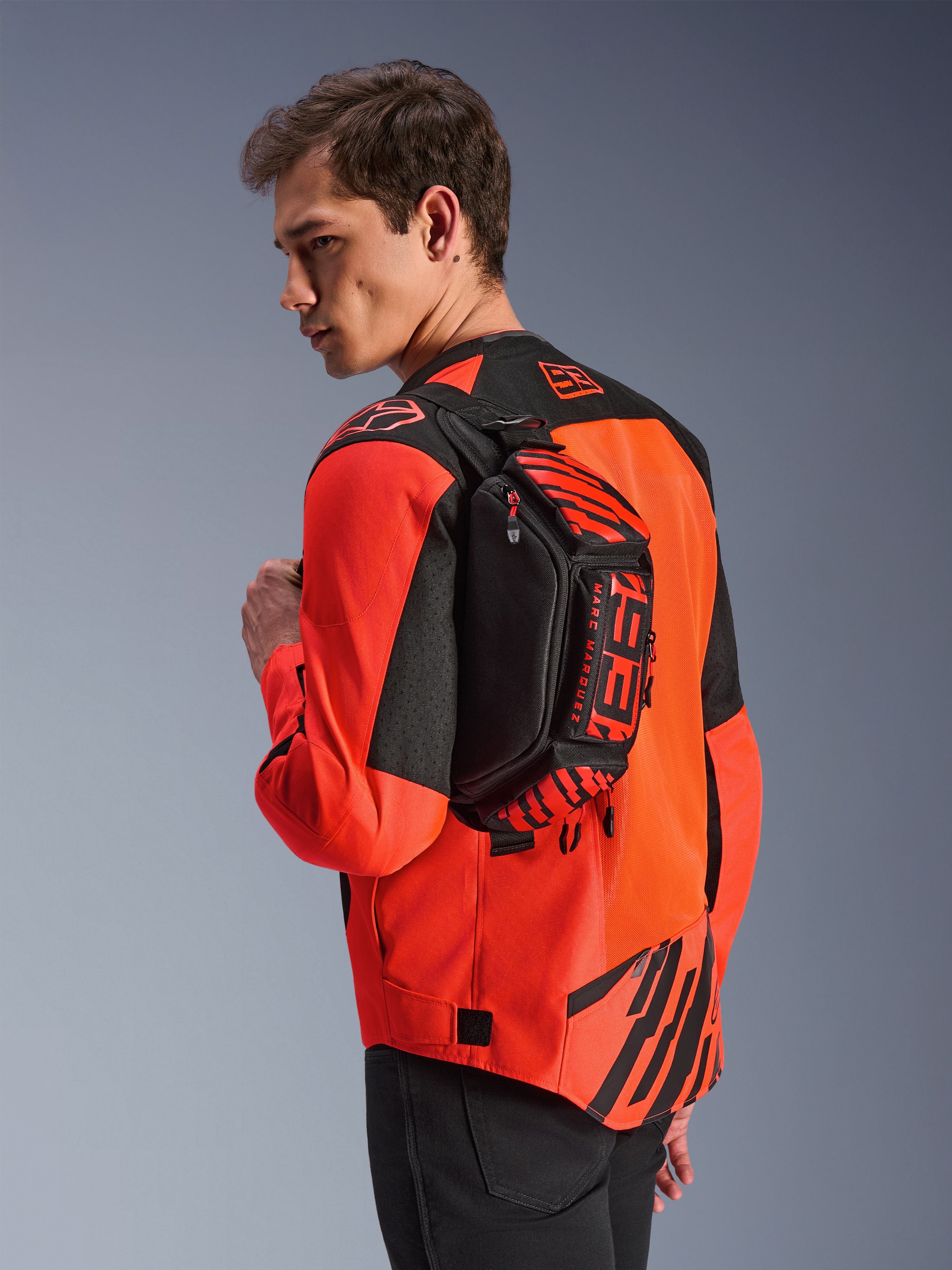 Alpinestars MM93 Waist Bag, Black with Red Fluo and Bright Red, worn by a model across the back over a red and black motorcycle jacket, featuring bold MM93 branding and Marc Marquez graphics