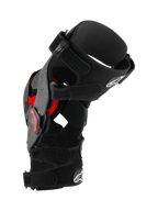 Rodillera Alpinestars Supertech RK-10 Plasma, protector de rodilla para motocross, negro y rojo, vista de perfil lateral que muestra la estructura de fibra de carbono forjada, correas ajustables e inserciones rojas de Nucleon PLASMA, equipo de protección para carreras off-road