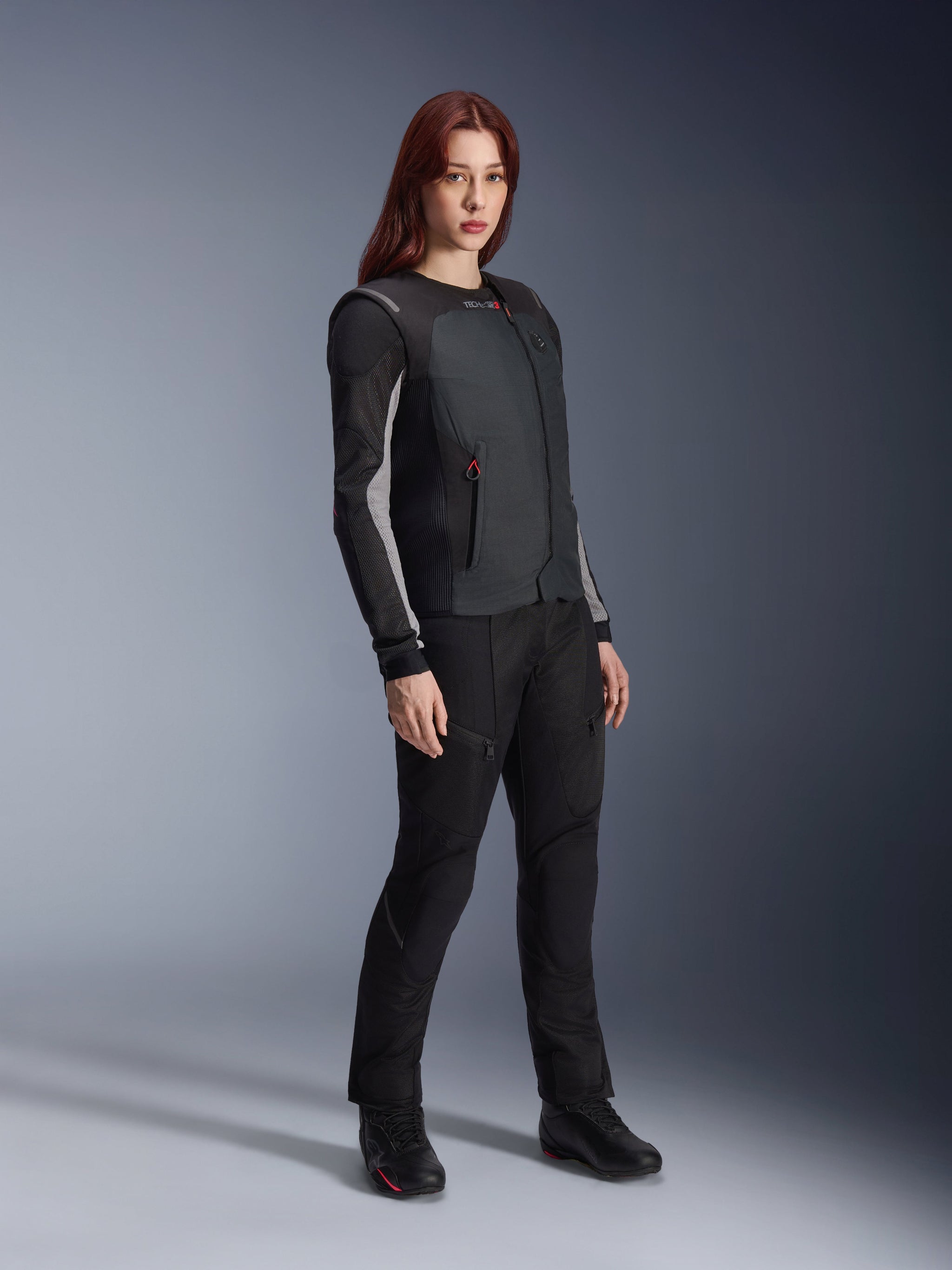 Alpinestars Stella Tech-Air 3 V2 System, chaleco airbag autónomo para moto de mujer en color negro, combinado con pantalones textiles de pilotaje y botas negras, con un ajuste entallado para protección urbana y de turismo