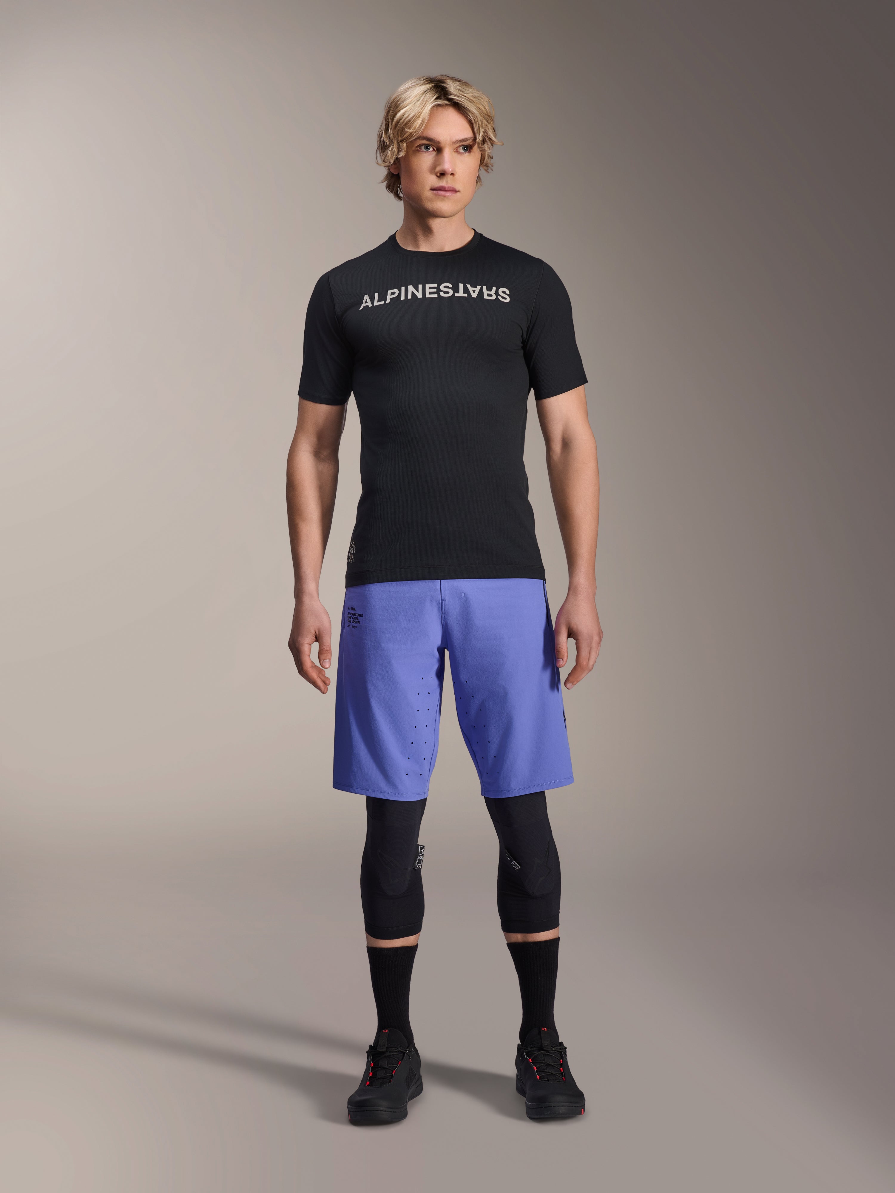 Alpinestars A-Aria Lite Short in Baja Blue, Men's MTB Shorts, worn with a black short-sleeve jersey and protective knee guards, featuring laser perforations for ventilation, mountain bike performance gear
