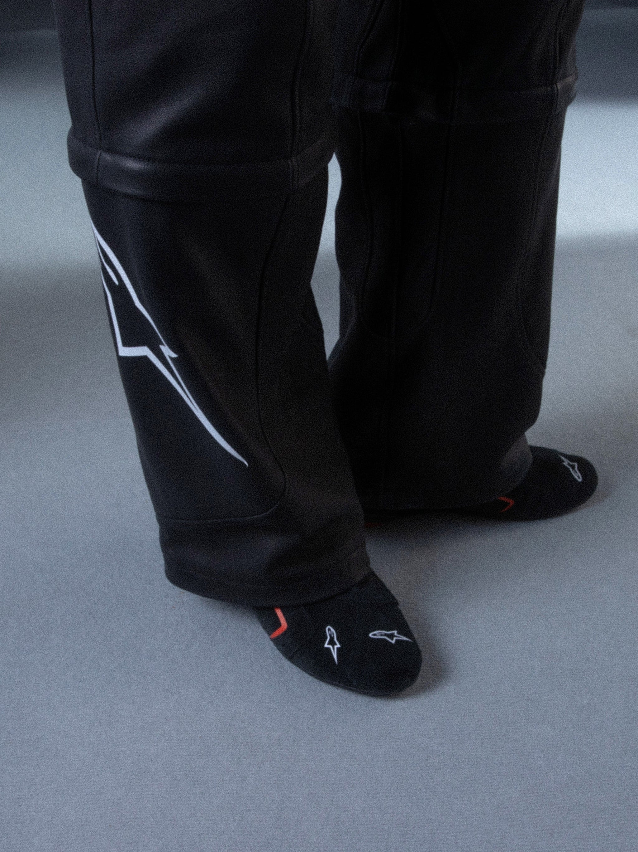 Alpinestars RSRV Starline Shoes, pantalones negros con líneas gráficas blancas laterales, calcetines negros con diseños rojos y blancos, textura suave y brillante
