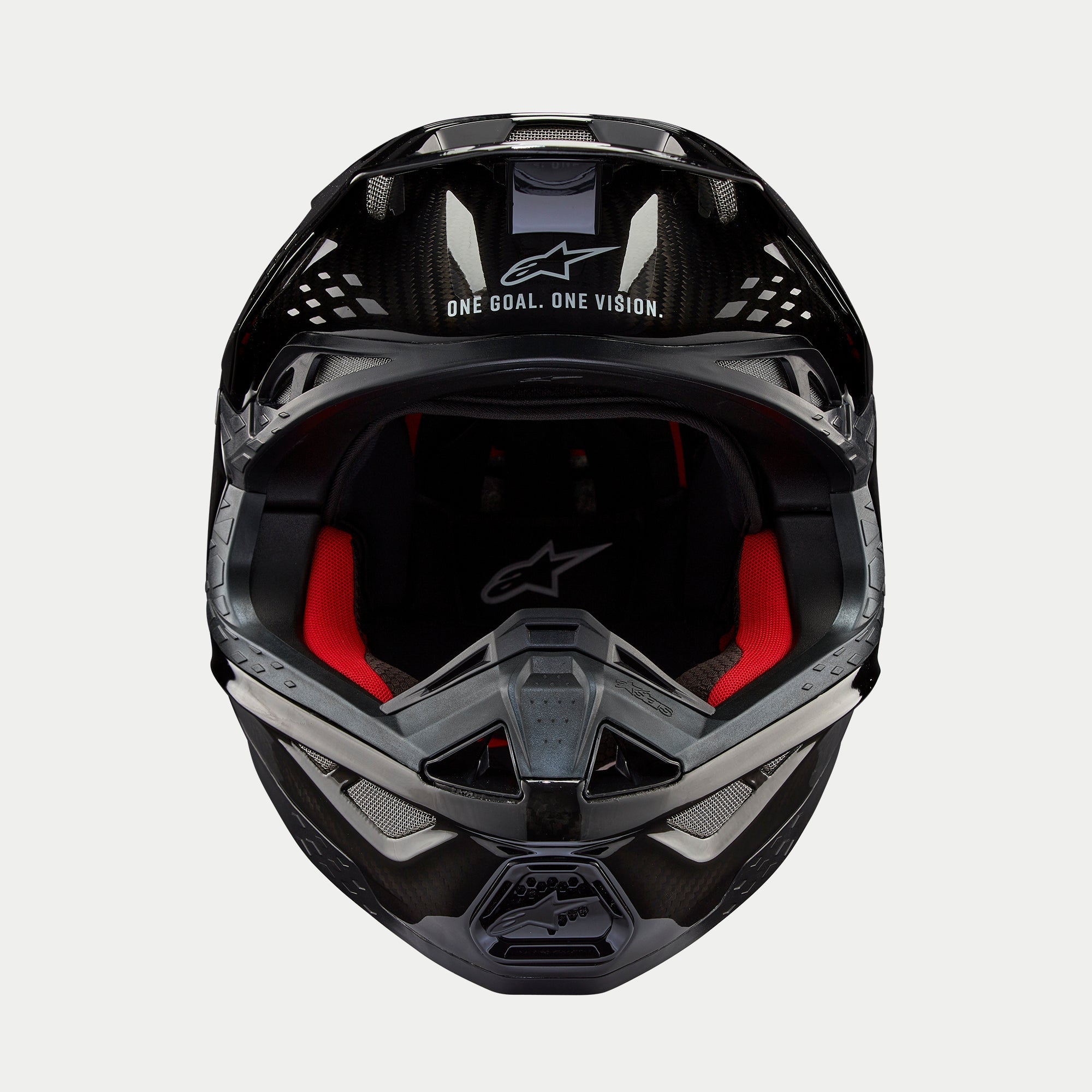 Casco Alpinestars Supertech M10 Solid, casco de motocross, carbono negro brillante, vista frontal que muestra el forro interior rojo, calota de fibra de carbono y el eslogan «ONE GOAL. ONE VISION.» en el área de la visera