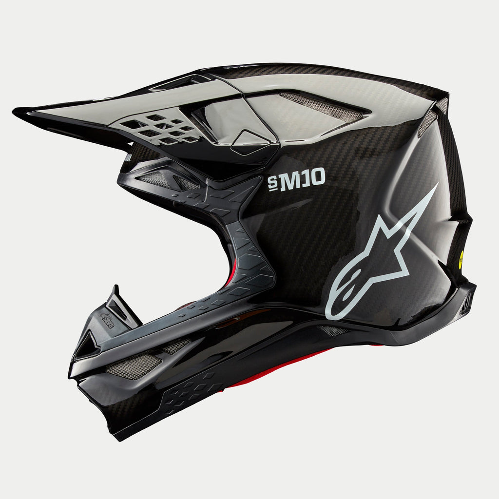 Casco Alpinestars Supertech M10 Solid, casco de motocross, carbono negro brillante, perfil lateral con tejido de fibra de carbono a la vista, marca SM10 y logotipo de Alpinestars en blanco, diseño aerodinámico estilizado con puertos de ventilación cubiertos de malla