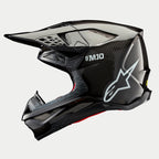 Casco Alpinestars Supertech M10 Solid, casco de motocross, carbono negro brillante, perfil lateral con tejido de fibra de carbono a la vista, marca SM10 y logotipo de Alpinestars en blanco, diseño aerodinámico estilizado con puertos de ventilación cubiertos de malla