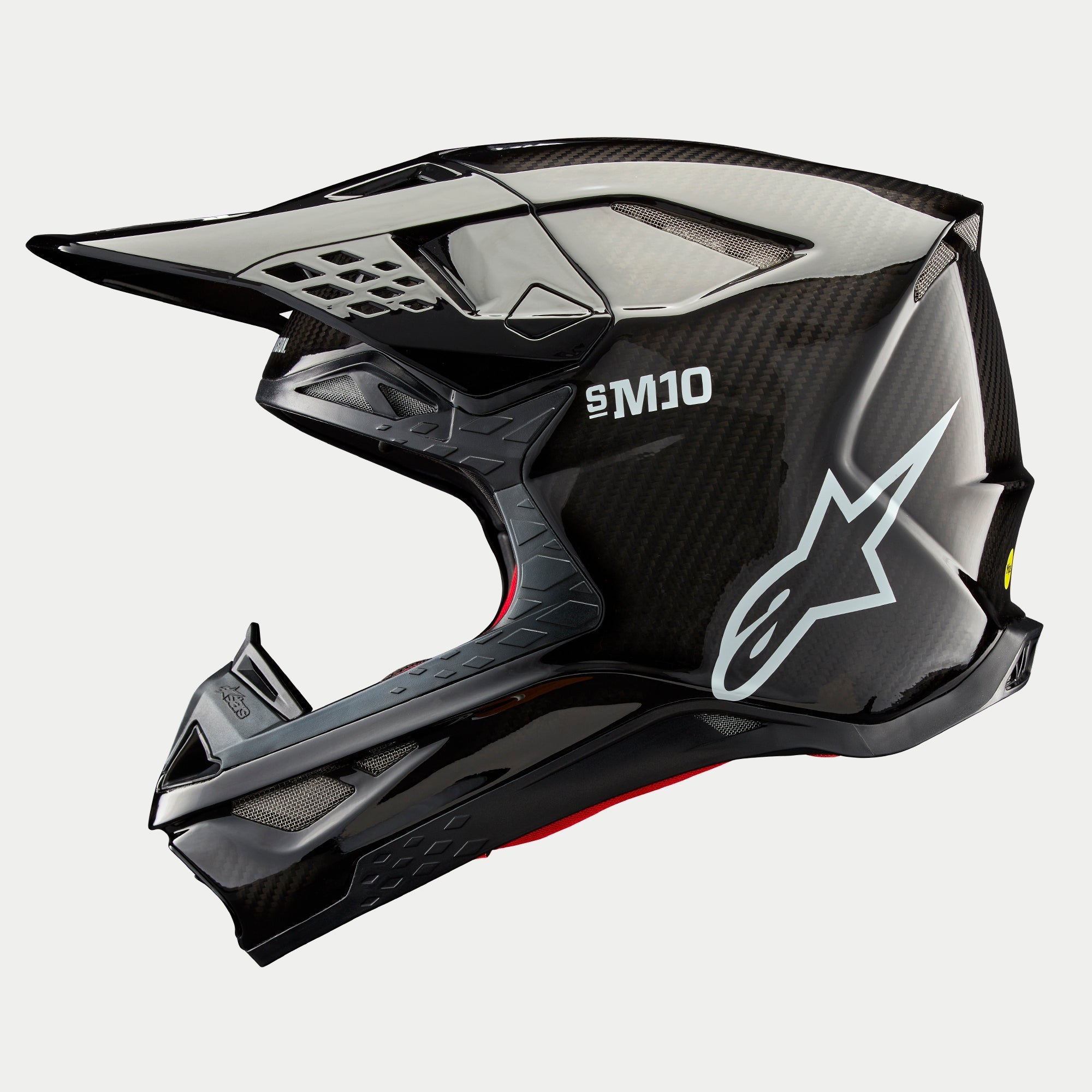 Casco Alpinestars Supertech M10 Solid, casco de motocross, carbono negro brillante, perfil lateral con tejido de fibra de carbono a la vista, marca SM10 y logotipo de Alpinestars en blanco, diseño aerodinámico estilizado con puertos de ventilación cubiertos de malla