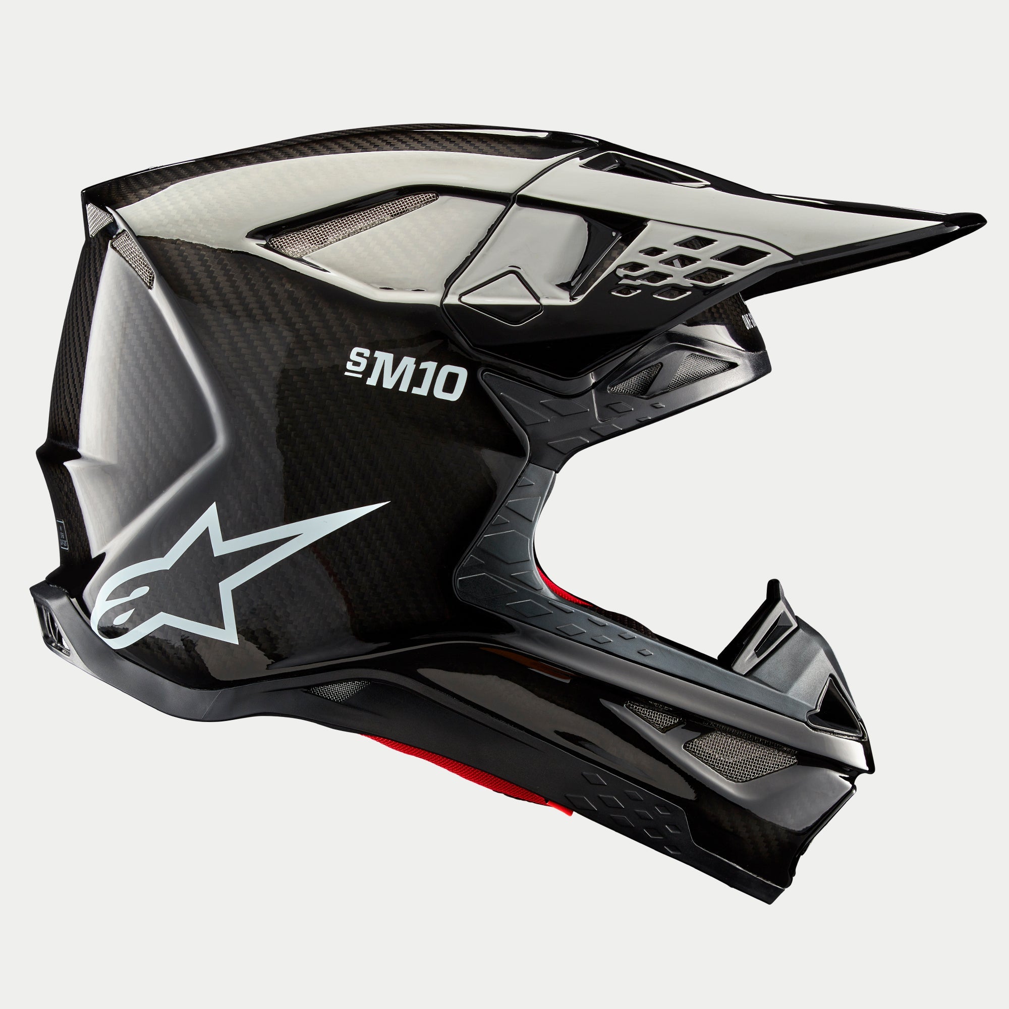 Casco Alpinestars Supertech M10 Solid, carbono negro brillante, casco de motocross, vista de perfil lateral que muestra el tejido de fibra de carbono brillante, marca S-M10, logotipo de la estrella de Alpinestars en blanco, diseño aerodinámico con visera y puertos de ventilación
