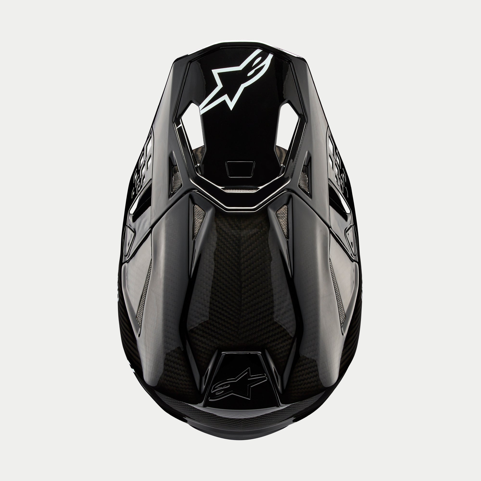 Casco Alpinestars Supertech M10 Solid, casco de motocross, carbono negro brillante, vista superior que muestra el tejido de fibra de carbono visible, logotipo blanco de Astars en la visera, perfil aerodinámico estilizado con puertos de ventilación integrados