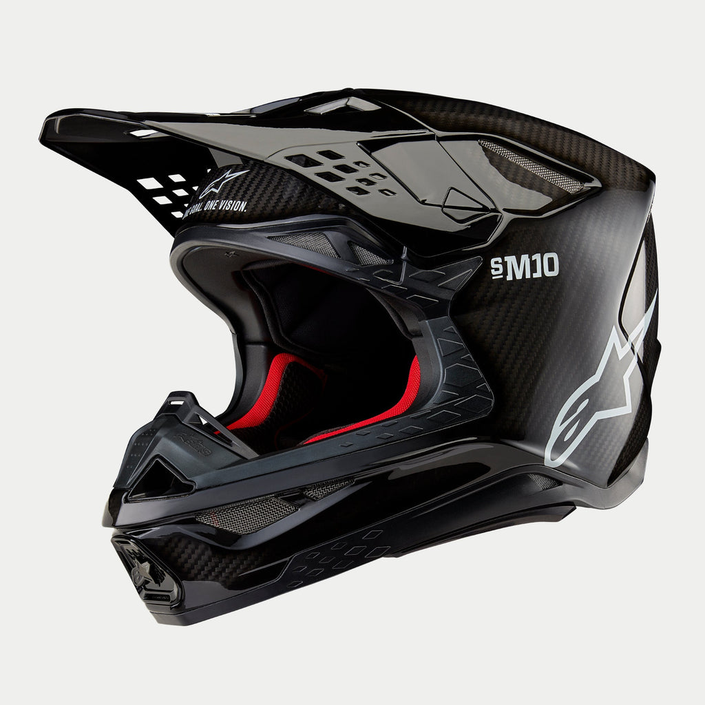 Alpinestars Supertech M10 Solid Helmet, casco de motocross, carbono negro brillante con tejido de fibra visible, logo blanco de Alpinestars y marca SM10, forro interior rojo, diseño aerodinámico con múltiples puertos de ventilación