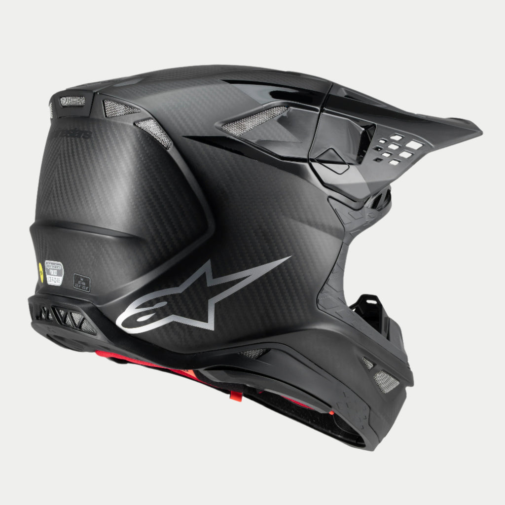Casco Alpinestars Supertech M10 Fame, casco de motocross, carbono negro mate y brillante, vista de tres cuartos trasera con textura de fibra de carbono visible, logotipo plateado y múltiples puertos de ventilación integrados, protección avanzada para la cabeza en conducción off-road