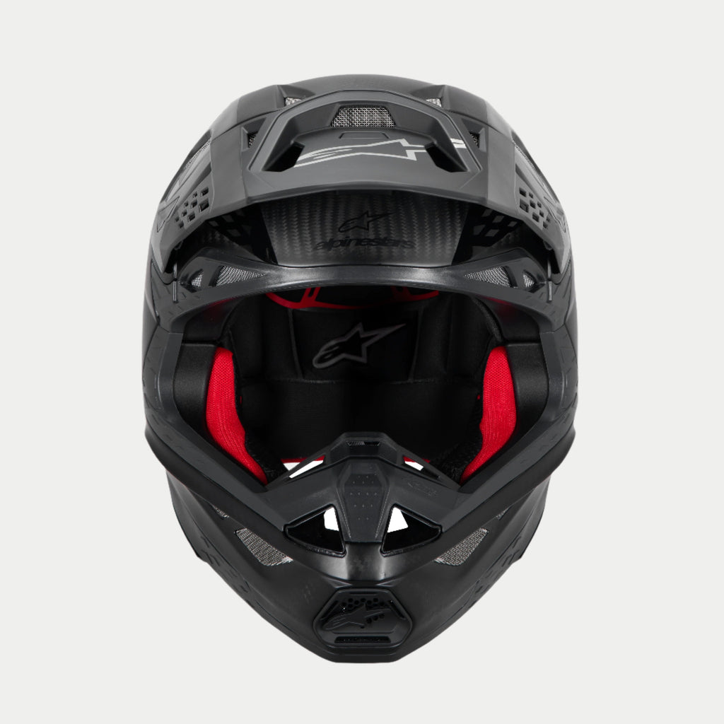 Casco Alpinestars Supertech M10 Fame ECE 22.06, casco de motocross, negro carbono mate y brillante, vista frontal con acolchado interior rojo visible, carcasa de fibra de carbono aerodinámica, diseño ventilado para carreras todoterreno