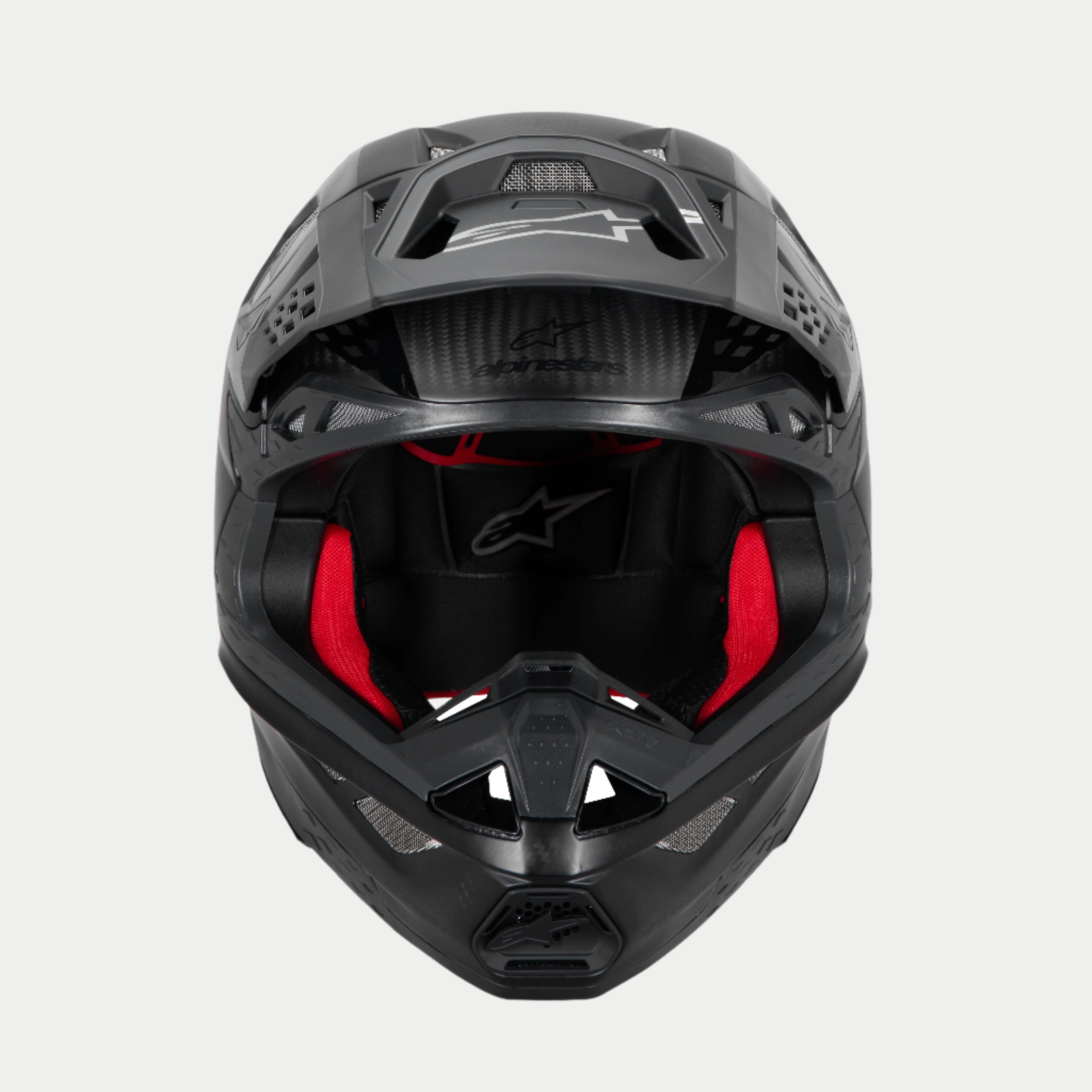Casco Alpinestars Supertech M10 Fame ECE 22.06, casco de motocross, negro carbono mate y brillante, vista frontal con acolchado interior rojo visible, carcasa de fibra de carbono aerodinámica, diseño ventilado para carreras todoterreno