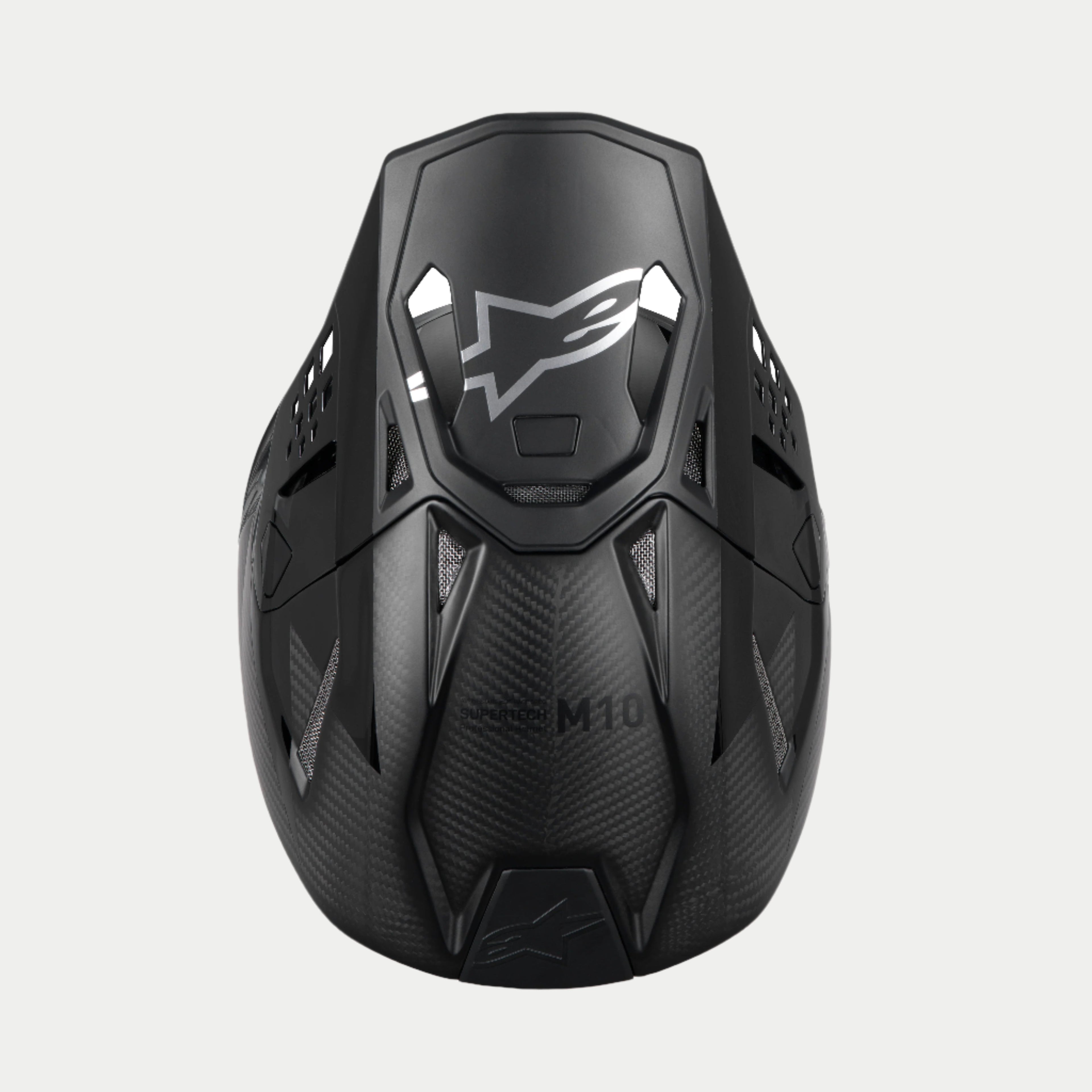 Casco Alpinestars Supertech M10 Fame ECE 22.06, casco de motocross, carbono negro mate y brillante, vista superior que resalta el tejido de fibra de carbono, visera aerodinámica con logotipo plateado de Alpinestars y múltiples puertos de ventilación para carreras todoterreno.