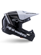 Casco Alpinestars S-M3 Radium, casco de motocross off-road, negro, blanco y gris brillante, con un diseño aerodinámico angular y puertos de ventilación, vista de perfil lateral, acabado brillante con franjas grises y visera blanca con el logotipo de Alpinestars