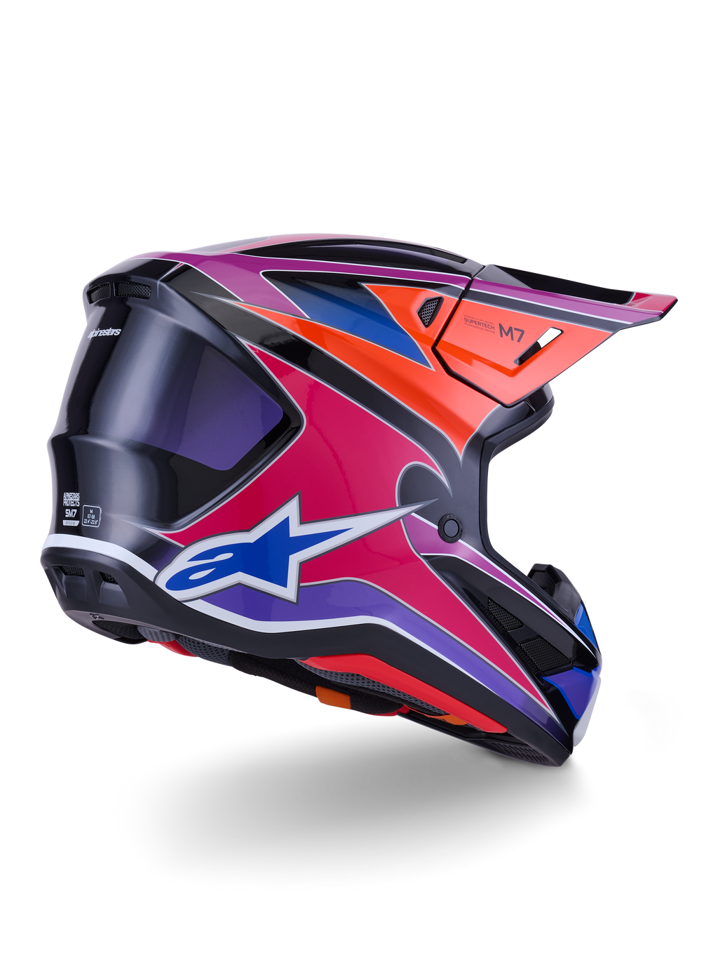 Casco Alpinestars S-M7 Fuse, casco de motocross, acabado brillante en azul, púrpura y rosa con detalles en naranja y negro, vista trasera en tres cuartos que muestra la calota aerodinámica, la visera y los puertos de ventilación, protección profesional para carreras off-road
