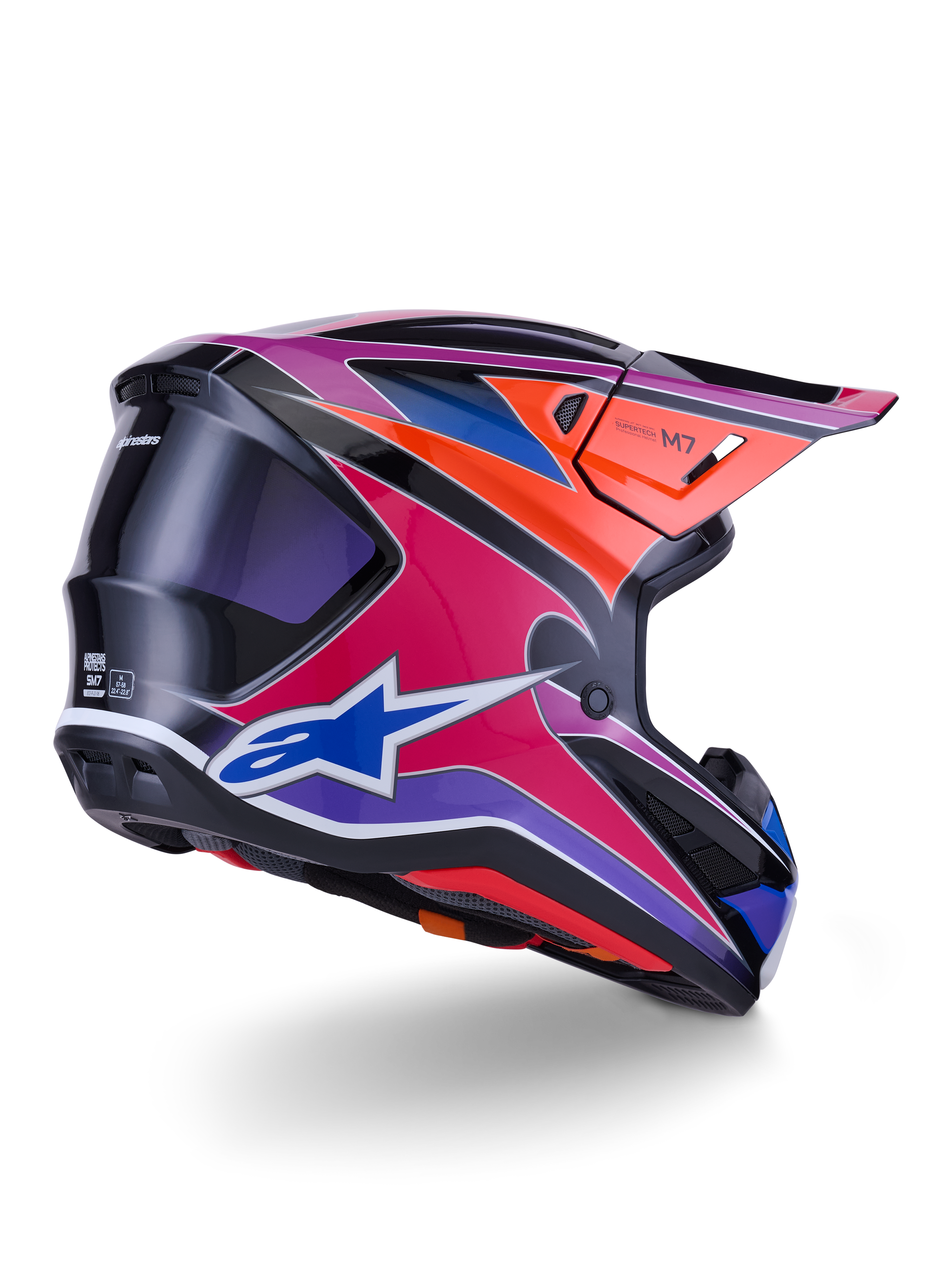 Casco Alpinestars S-M7 Fuse, casco de motocross, acabado brillante en azul, púrpura y rosa con detalles en naranja y negro, vista trasera en tres cuartos que muestra la calota aerodinámica, la visera y los puertos de ventilación, protección profesional para carreras off-road